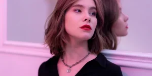Stylish woman with red lips and necklace reflecting in mirror indoors