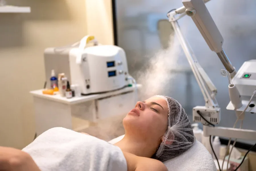 El procedimiento de vaporizar la piel de la cara de una mujer joven antes de limpiar la piel en un salón de belleza.
