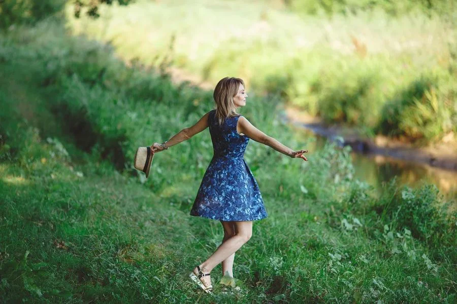 Frau steht mit ausgebreiteten Armen auf einer Wiese