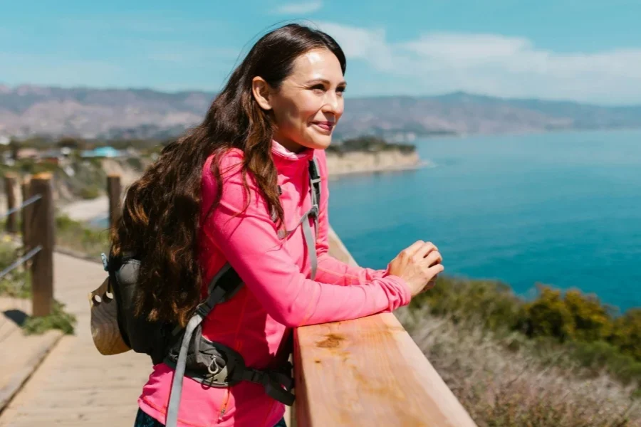 Mujer con chaqueta rosa de pie en un muelle de madera marrón