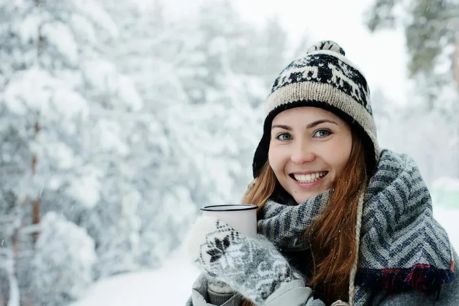 Mujer sonriendo mientras sostiene una taza y está de pie en la nieve