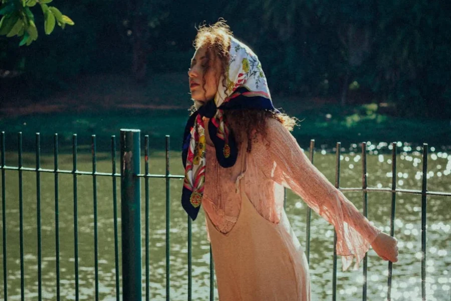 Кудрявая девушка в атласном шарфе позирует за забором