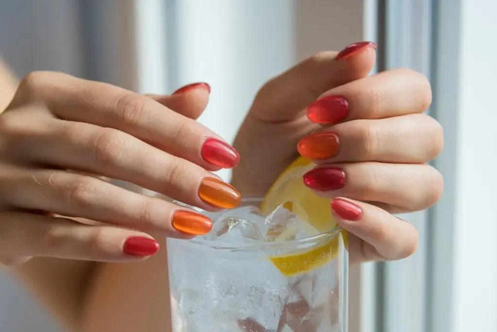 Glänzende Jelly-Nägel in leuchtendem Rot mit natürlicher Transparenz, gepaart mit einem Fruchtscheibenglas
