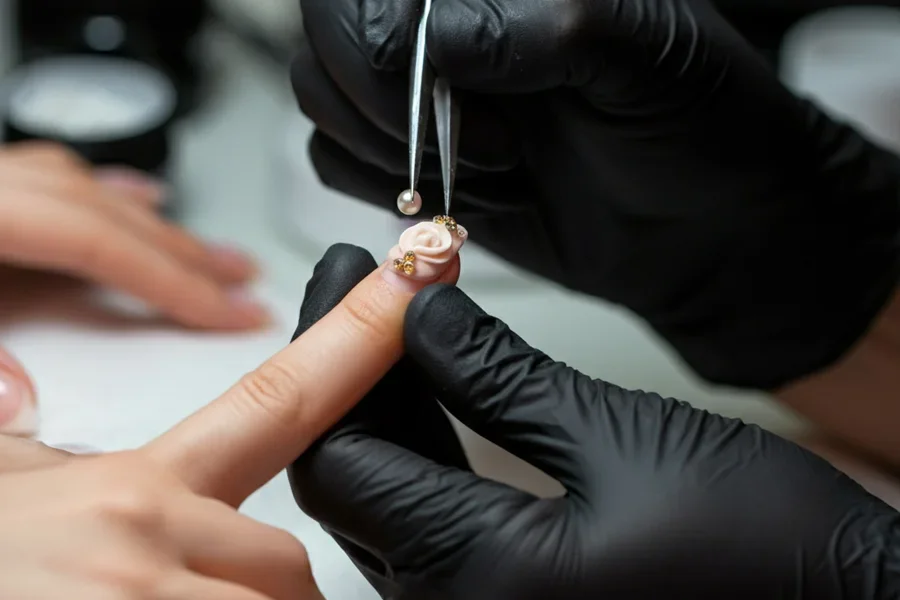 El artista de uñas coloca meticulosamente pequeñas perlas sobre un detalle floral de gel 3D para lograr un arte de uñas inspirado en joyas.