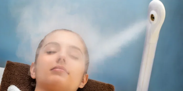 up portrait of young woman with eyes closed having thermal steam treatment on face. Girl wearing white gown laying on couch in spa