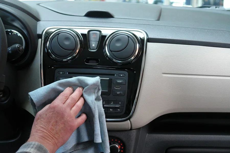 A gray towel being used to wipe buttons on a car's dashboardcenter console