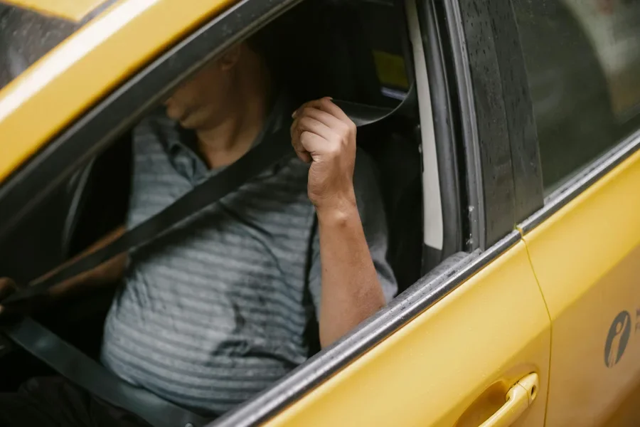 A man securely fastens his seatbelt inside a yellow taxi, emphasizing safety during urban transport