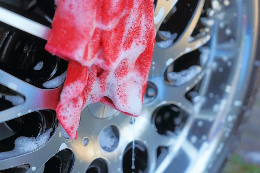 A red towel being used to wipe a car wheel hub