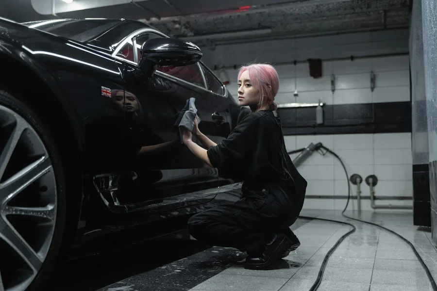 A young female worker polishing a black luxury car in an indoor garage setting