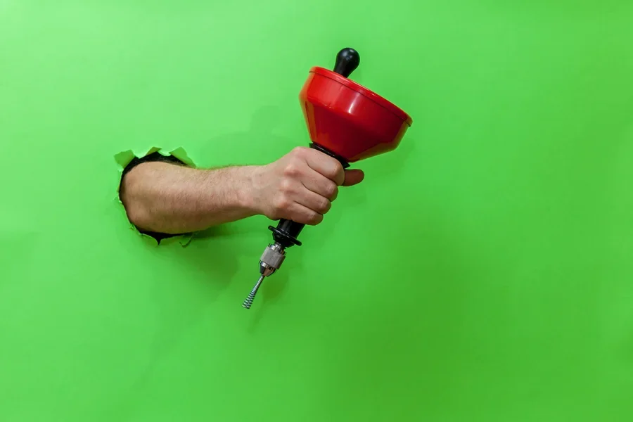 Arm punched through green wall holding drain snake tool