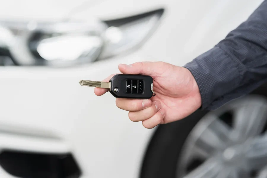 Крупный план: ключи от машины и пульт дистанционного управления автомобильной сигнализацией, держащийся в руке