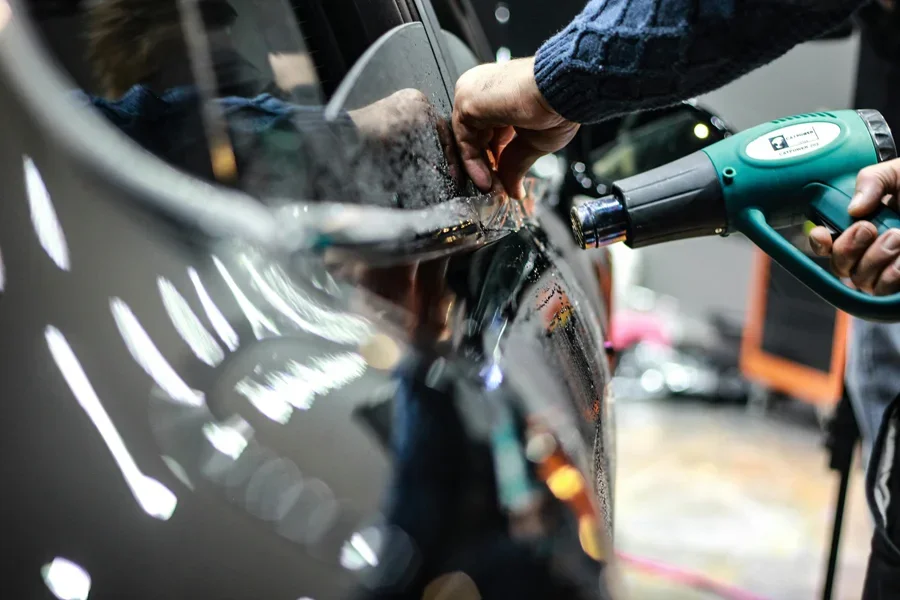 Close-up of a worker using a heat gun for car detailing in an indoor garage setting