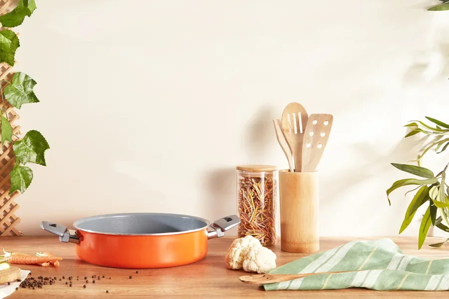 Panci oranye dengan dua pegangan diletakkan di atas meja kayu