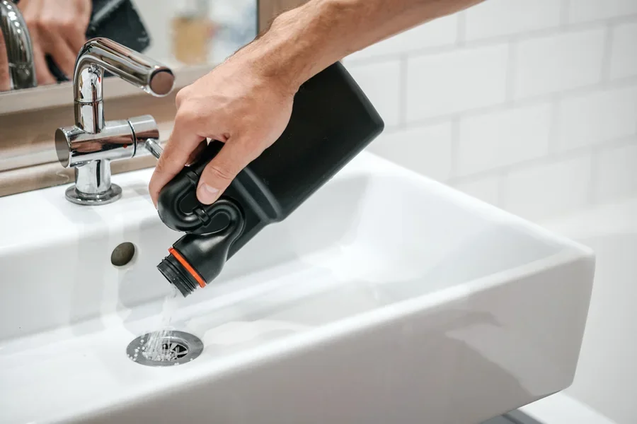 Person pouring drain cleaner down white bathroom sink