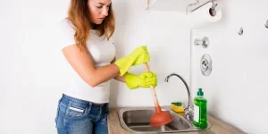 Woman in kitchen using rubber plunger on sink’s drain