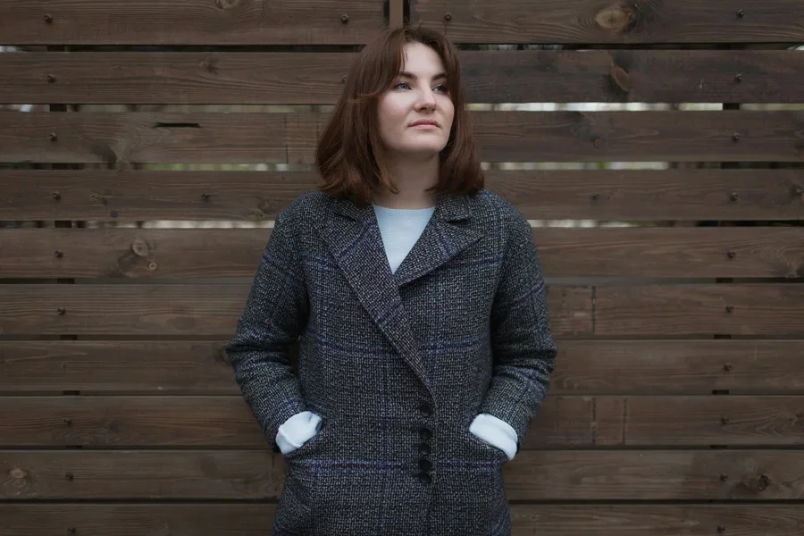 Frau im blau-weiß gepunkteten Mantel steht neben einer braunen Holzwand