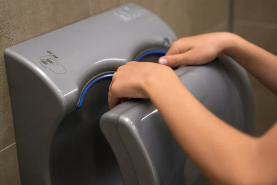 Young Boy Dries Wet Hands with an Electric Hand Dryer