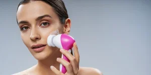 Mujer joven usando un cepillo electrónico de limpieza facial