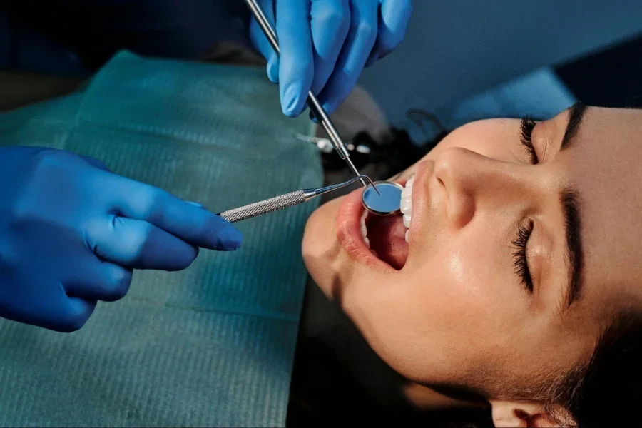 A Person Wearing Blue Latex Gloves Holding a Mirror in a Woman's Mouth