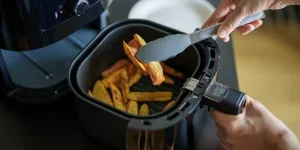 A woman is using an air fryer to prepare food in her kitchen