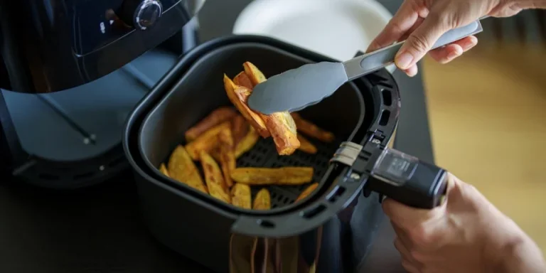 A woman is using an air fryer to prepare food in her kitchen