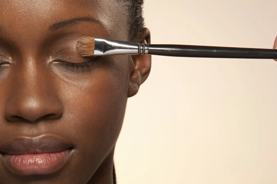 Dark skinned woman using brush to apply natural eyeshadow color