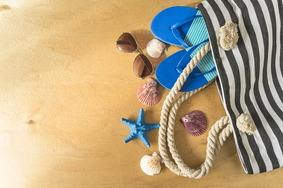 Sac de plage en tissu d'où tombent chaussures et lunettes de soleil