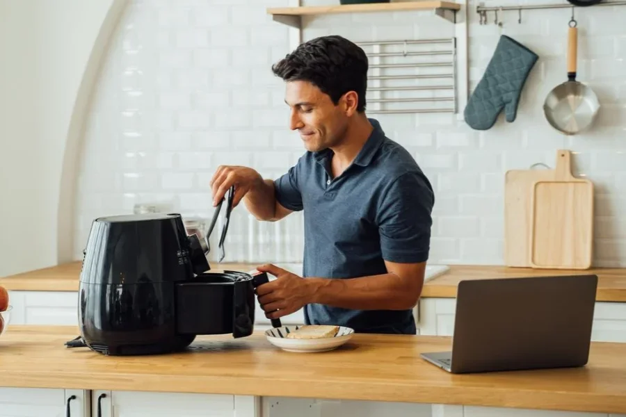 Hombre usando una freidora de aire y una computadora portátil en la cocina