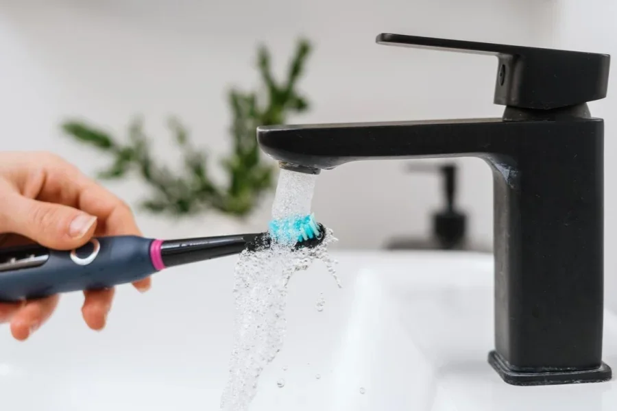 Woman holding modern toothbrush under flowing water from mixer