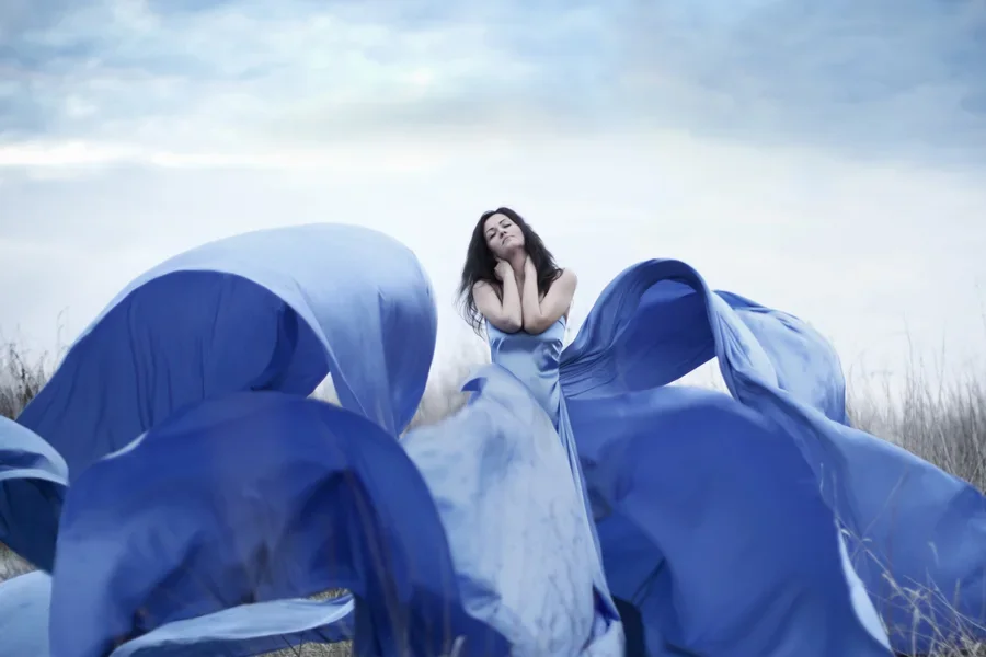 Woman in blue dress with dreamlike waves standing in grass
