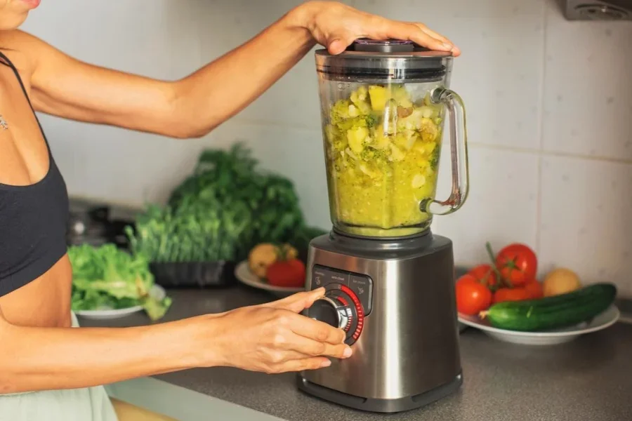 Женщина готовит сливочный суп из овощей в блендере.