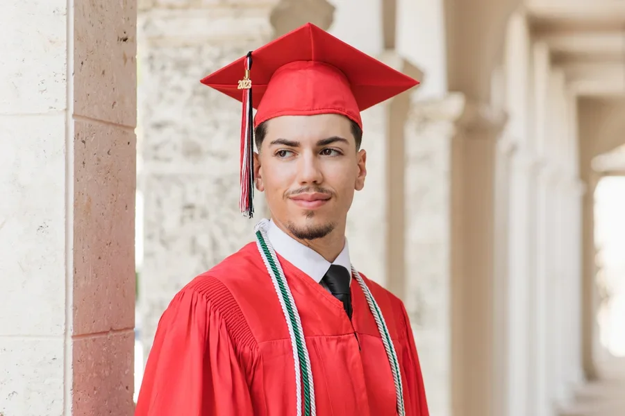 Un joven con un birrete de graduación decorado en rojo en el pasillo