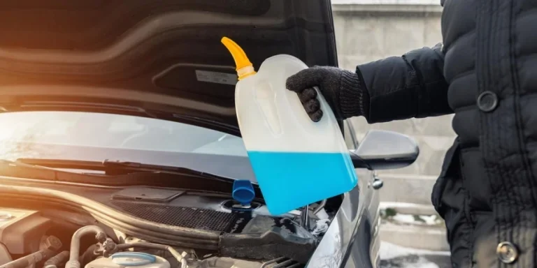 Крупный план руки водителя или механика в перчатках, льющей синюю антифризную жидкость для зимней мойки лобового стекла автомобиля водой из бутылки.