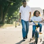 Un homme debout à côté de sa femme apprend à leur enfant à faire du vélo