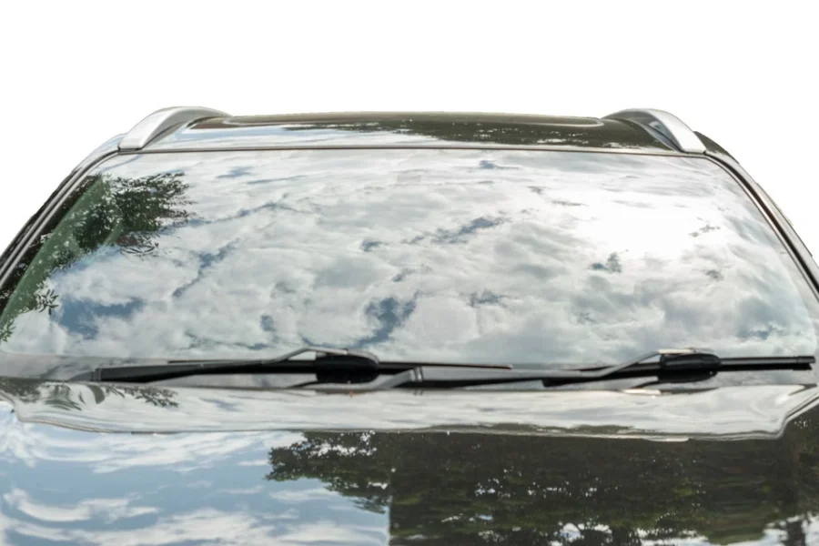 Voiture moderne garée sur fond blanc, ciel bleu et nuages ​​se reflétant dans le pare-brise.
